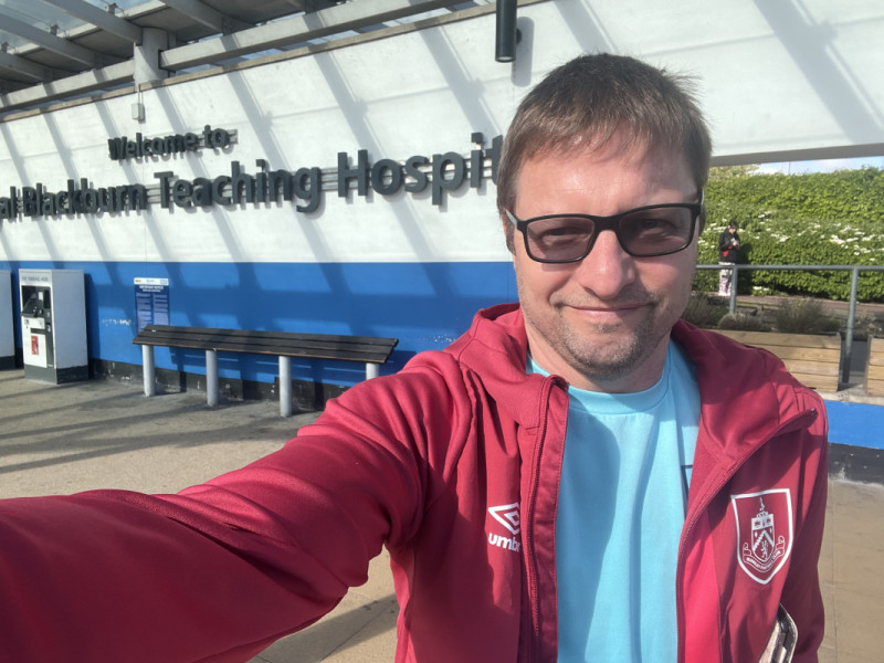 Me, stood in front of the Royal Bl@ckburn Hospital entry banner, in a branded claret Burnley soft shell and turquoise Burnley training top.